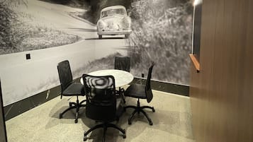 Ein Konferenzraum mit rundem Tisch und vier Stühlen, einem Wandgemälde eines Oldtimers und einer Holzwand rechts.