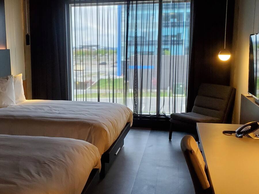 A hotel room with two beds, a desk, a chair, a TV, and a window with a view of the outside.