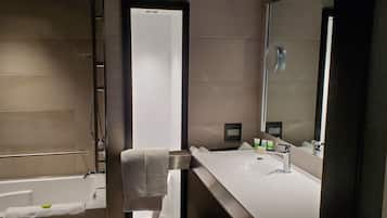 A modern bathroom with a large mirror, a bathtub, and a vanity with a sink.