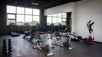 A gym with various exercise equipment, large windows, and a view of the outdoors.