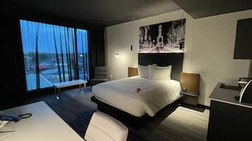 Quarto de hotel moderno com uma cama grande, uma escrivaninha e vista para o horizonte urbano pela janela.