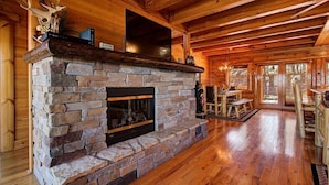 A stone fireplace with a television above it, wooden floors, and a dining area with a table and chairs. - Great Peaks View☀ HotTub, Game room, Theater, 10 min to Parkway, Mountain Views  (Sevierville)