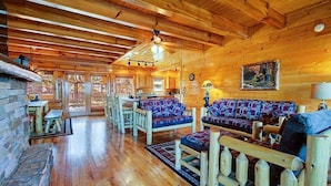 A log cabin interior with a wooden floor, a sofa set, a dining table, and a fireplace. - Great Peaks View☀ HotTub, Game room, Theater, 10 min to Parkway, Mountain Views  (Sevierville)