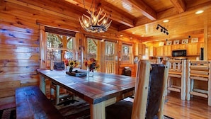A wooden cabin interior with a dining table, chairs, a chandelier, and a kitchen area. - Great Peaks View☀ HotTub, Game room, Theater, 10 min to Parkway, Mountain Views  (Sevierville)