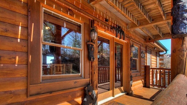 A log cabin with large windows, a wooden porch, and a bear sculpture. - Great Peaks View☀ HotTub, Game room, Theater, 10 min to Parkway, Mountain Views  (Sevierville)