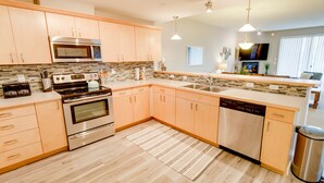 A modern kitchen with stainless steel appliances, wooden cabinets, and a tiled backsplash. - Seagulls Nest Condominium - Oyhut Bay Seaside Village (Ocean Shores)