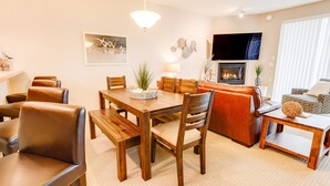 A cozy living room with a wooden dining table, leather chairs, a fireplace, and a flat-screen TV. - Seagulls Nest Condominium - Oyhut Bay Seaside Village (Ocean Shores)