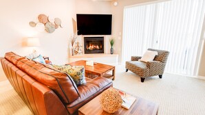 A living room with a leather sofa, patterned armchair, and a fireplace. - Seagulls Nest Condominium - Oyhut Bay Seaside Village (Ocean Shores)
