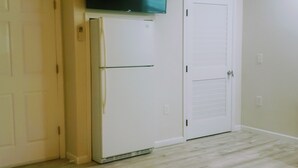 A room with a white refrigerator, a white door, and a wall-mounted television.