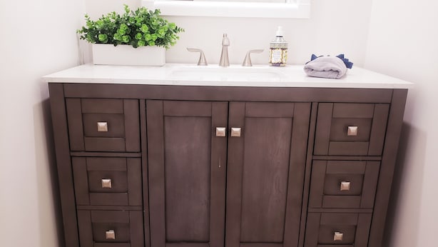 A dark brown vanity with a white countertop, a potted plant, a soap dispenser, and a towel.