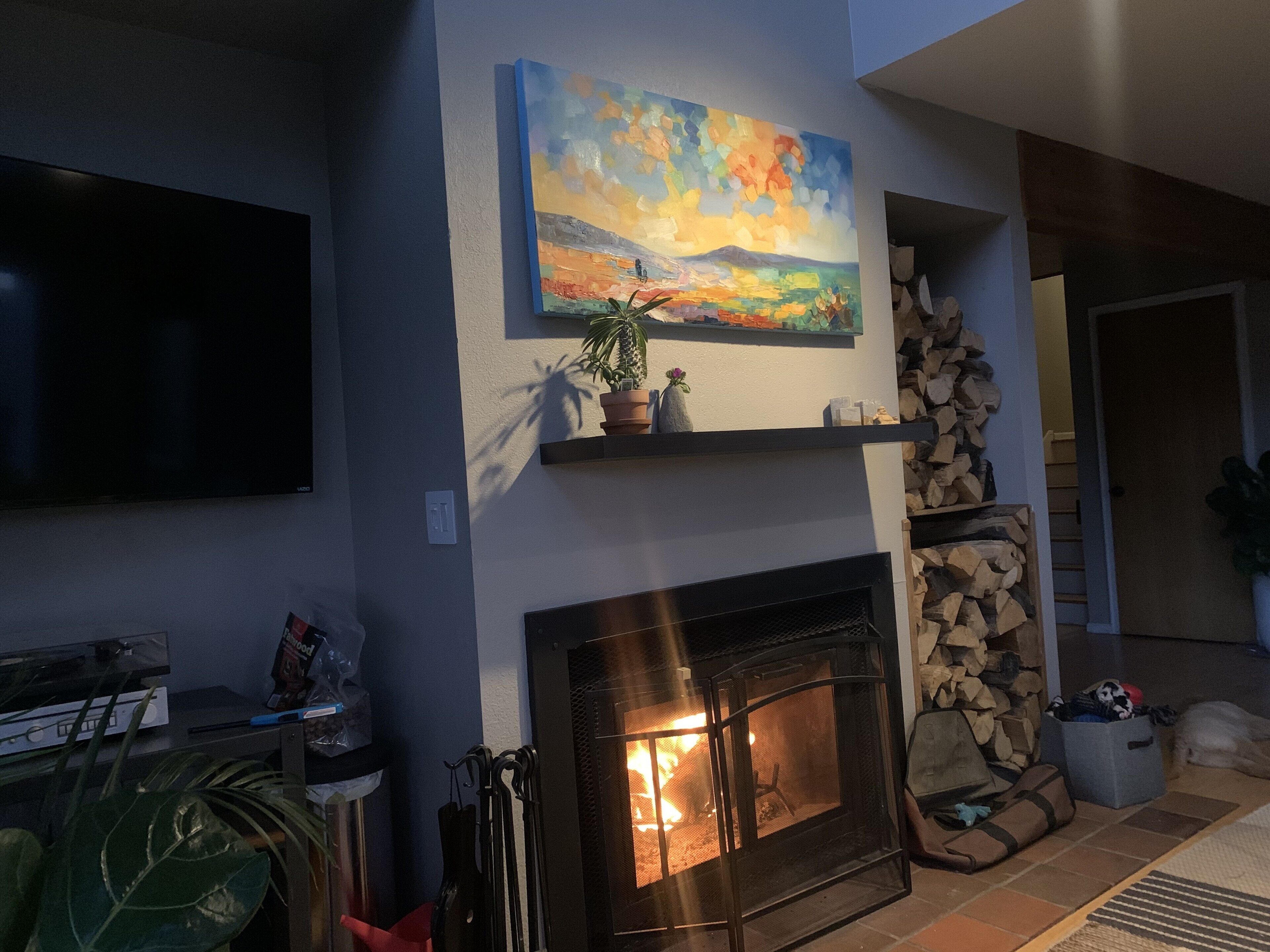 Un salon avec une cheminée, un téléviseur fixé au mur et un tableau accroché au mur.