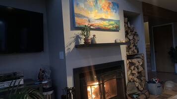 Un salon avec une cheminée, un téléviseur fixé au mur et un tableau accroché au mur.
