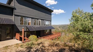 Una casa moderna de dos pisos con paneles solares, una terraza de madera y una vista panorámica a las montañas.