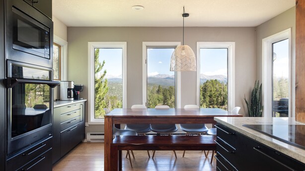 Una cocina moderna con una mesa de comedor de madera, armarios negros y grandes ventanas con vistas a la montaña.