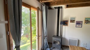 A room with a wooden ceiling, a window with curtains, a small stove, and a table.