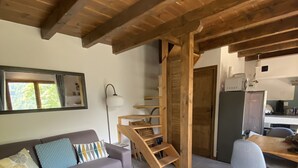 A modern living room with a wooden ceiling, a sofa with patterned cushions, a wooden coffee table, and a staircase leading to another level.