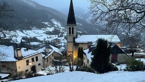 A snow-covered village with a prominent church steeple, traditional buildings, and a mountainous backdrop.