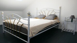 Una cama con estructura metálica blanca y detalles dorados, una mesita de noche con lámpara, y una ventana sobre la cama.