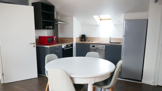 Cocina compacta con una mesa y sillas blancas, un microondas rojo y un horno empotrado.