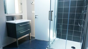 Un baño moderno con ducha de vidrio, tocador de tonos oscuros con cajones y un espejo grande sobre el lavamanos.