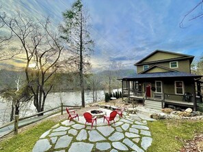 A lakeside house with a stone patio, red chairs, and a gazebo. - Delightful riverview house with screened porches (Hot Springs)