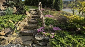 Un chemin de pierres qui mène à une maison entourée d’une végétation luxuriante et de grands arbres.