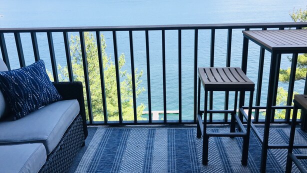 Un balcón con vista a un lago y colinas, con un sofá, una mesa y una silla.