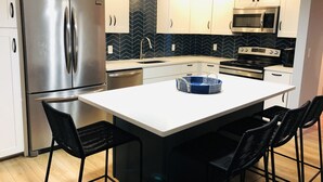 Una cocina moderna con armarios blancos, un refrigerador de acero inoxidable, un microondas y un protector contra salpicaduras en diseño espiga.