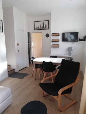 A modern dining area with a white table, black chairs, and a TV mounted on the wall.