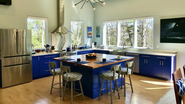Una cocina moderna con una isla central, taburetes de bar y un refrigerador de acero inoxidable.