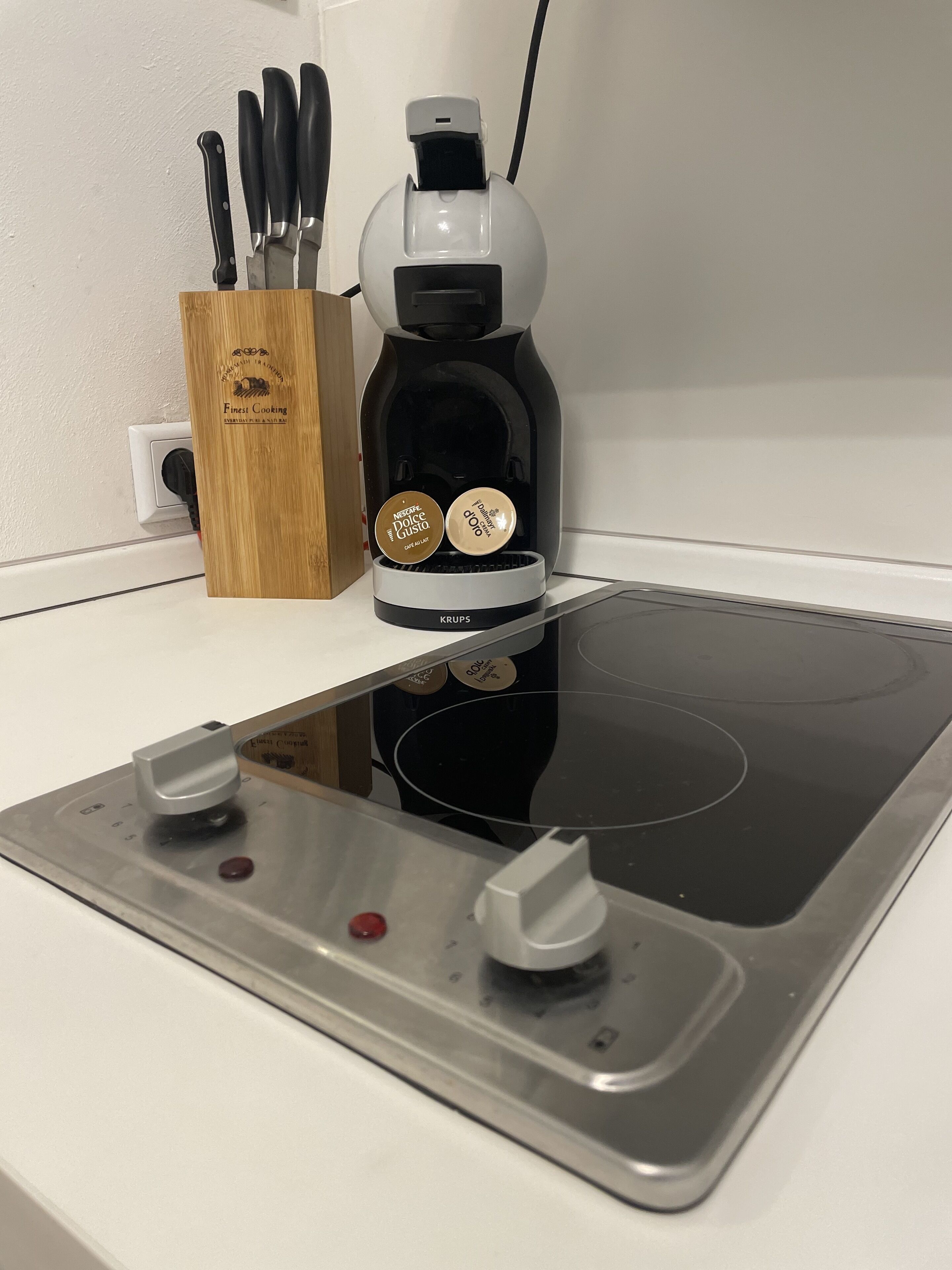A kitchen with a black coffee maker, a wooden knife block, and a stainless steel induction cooktop.