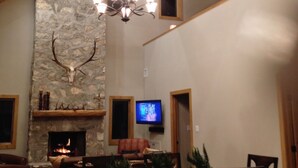 A spacious living room with a stone fireplace, wooden beams, a chandelier, and a television. - Hill Country Ranch Retreat (Johnson City)