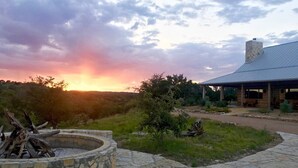 A stone fire pit, a covered outdoor seating area, and a building with a metal roof. - Hill Country Ranch Retreat (Johnson City)