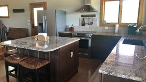 A kitchen with a central island, dark wood cabinets, stainless steel appliances, and a window with a view. - Hill Country Ranch Retreat (Johnson City)