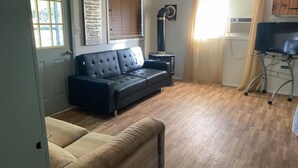 Ein Wohnzimmer mit einem dunkelbraunen Ledersofa, einem beigen Sessel, einem kleinen Beistelltisch und einem Fernseher auf einem Schrank.