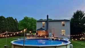 Una piscina con solárium, rodeada por una valla de madera y luces colgantes.