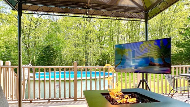 Un espacio al aire libre cubierto con una piscina, una fogata y una pantalla de televisión que muestra una escena de playa.