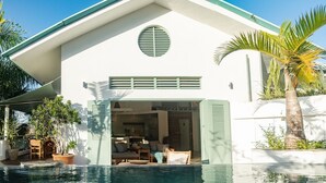 Une maison moderne dotée d’une piscine, d’un coin repas et d’une cuisine visible à travers la porte ouverte.