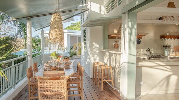 Une terrasse en bois avec une table et des chaises, un luminaire suspendu et une vue sur l’océan.