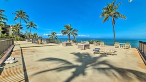 Een terras aan het strand met lounge stoelen en tafels, palmbomen en uitzicht op de oceaan.