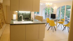 A modern kitchen with a central island, a dining area with yellow chairs, and large windows offering a view of greenery. - Luxury apartment in the olive grove in the hinterland of Alassio/Albenga, carport, Wifi (Casa nova Lerrone)