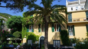 A building with a yellow facade, green shutters, and a palm tree in front. - Luxury apartment in the olive grove in the hinterland of Alassio/Albenga, carport, Wifi (Casa nova Lerrone)