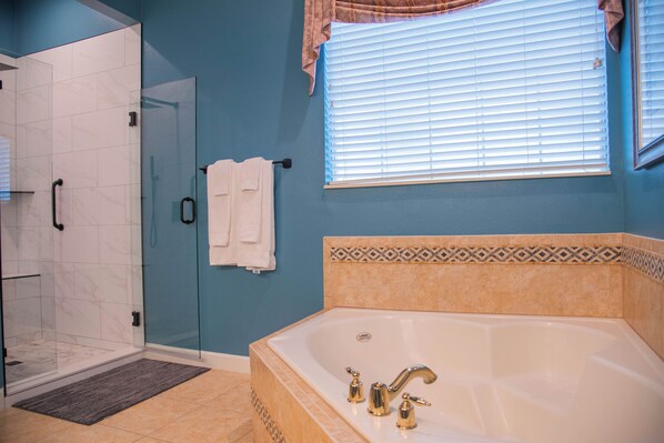 A bathroom with a glass shower enclosure, a bathtub with gold fixtures, and a window with blinds. - 5BR Reunion Villa with Private Pool & Spa (Kissimmee)