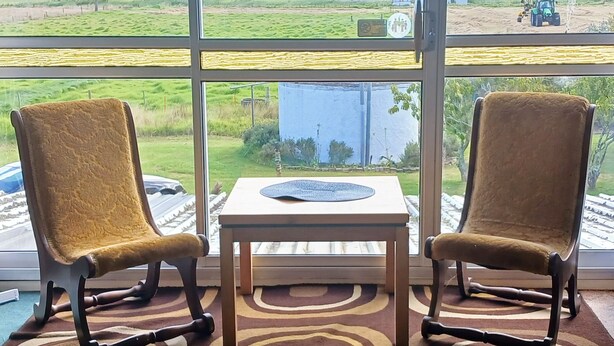 Une pièce avec deux chaises placées face à une grande fenêtre, une petite table et une vue sur un paysage rural.