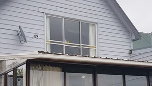 Une maison dotée d’un patio couvert, d’une grande fenêtre avec des rideaux et d’une antenne parabolique.