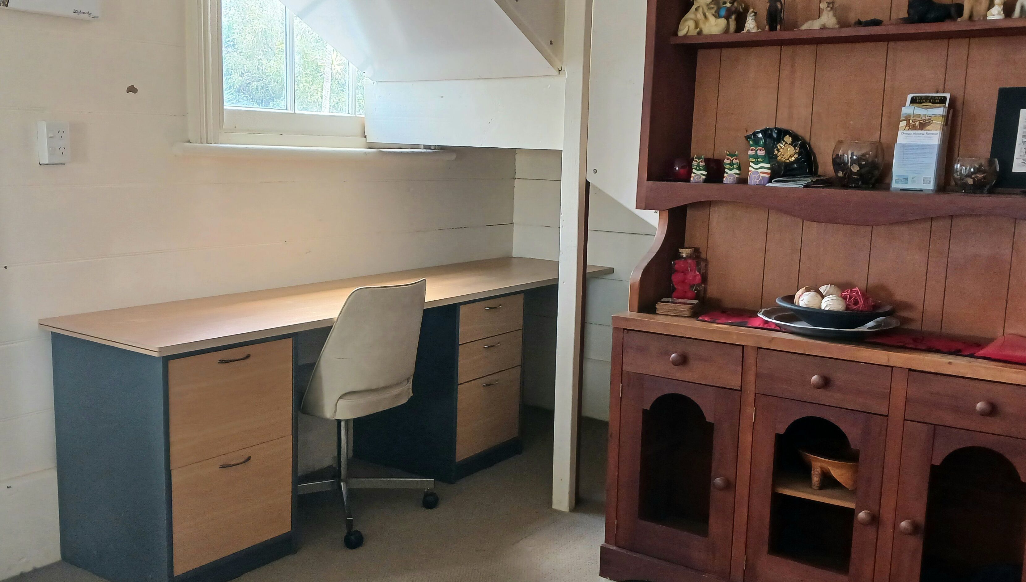 A small office with a desk, chair, and a wooden cabinet with decorative items.