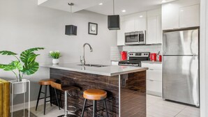 Une cuisine moderne dotée d’un îlot central, d’appareils électroménagers en acier inoxydable et de tabourets de bar.