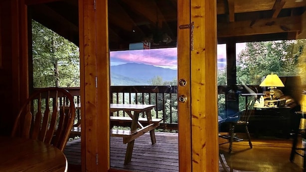 A wooden deck with a table and chairs, a view of a mountain and trees, and a yellow lamp on the right. - New Hot Tub, Outdoor Bar, Family Friendly, Awesome Views, Golf, Bears, Pool (Gatlinburg)
