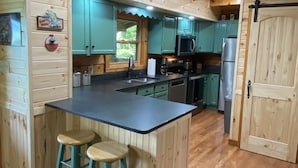 A wooden cabin kitchen with a central island, bar stools, teal cabinets, and modern appliances. - New Hot Tub, Outdoor Bar, Family Friendly, Awesome Views, Golf, Bears, Pool (Gatlinburg)