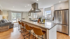 A modern kitchen with a large island, stainless steel appliances, and a grey sofa in the adjacent living area. - Serene Canyon Private Villa•Pool•HotTub•Sauna Retreat STR Permit Number:14614552 (Pacifica)